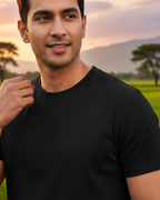 Man wearing a black t-shirt standing in a field with trees and mountains in the background