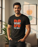 Man wearing a black t-shirt with 'DO WHAT YOU WANT' text in a room with a couch and plant.