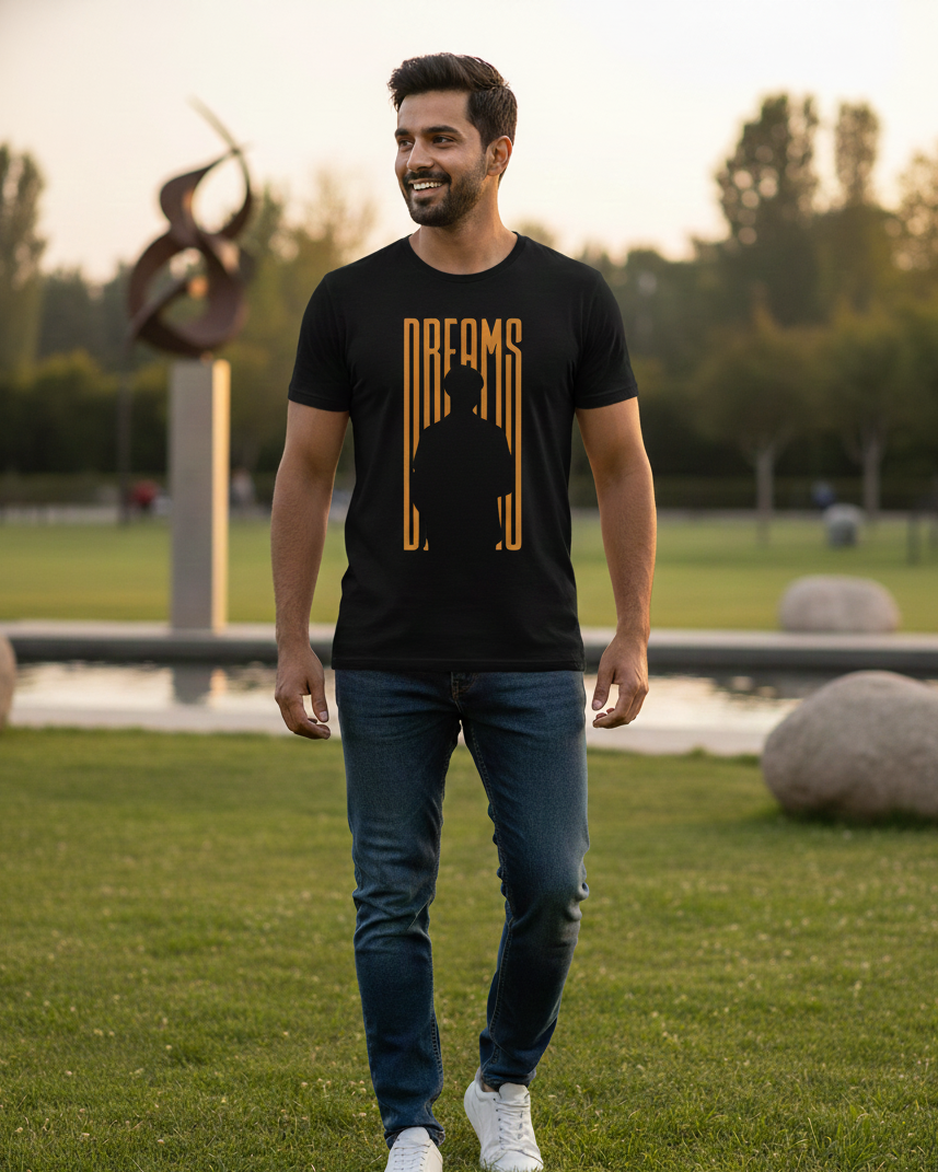 Man wearing a black t-shirt with 'DREAMS' printed on it, standing in a park