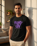 Man wearing a black t-shirt with purple text in a room with a couch and plants.