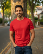 Man wearing a red t-shirt standing next to a tree on a street