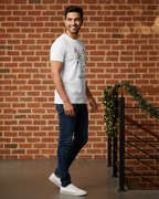 Man wearing a white t-shirt with a colorful design, standing in front of a brick wall.