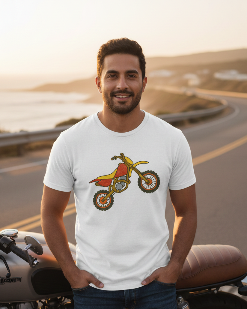 Man wearing a white t-shirt with a graphic design of a red and yellow dirt bike, standing on a road with a scenic background.