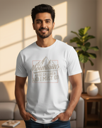 Man wearing a white t-shirt with a mountain design and text in a living room.