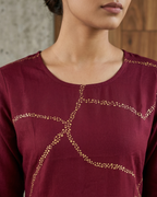 Maroon top with gold embellishments worn by a person, against a neutral background