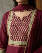 Maroon traditional outfit with intricate green and gold patterns on a neutral background