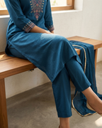 Person wearing a blue embroidered outfit sitting on a wooden bench.