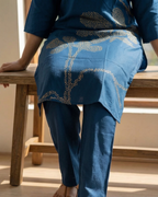 Person wearing a blue outfit with floral patterns sitting on a wooden bench.