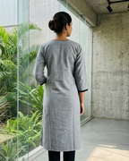 Person wearing a gray dress standing in a modern indoor setting with plants.