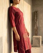 Person wearing a maroon traditional outfit with floral patterns against a concrete wall.