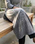 Person wearing a patterned gray and black garment sitting on a wooden bench.