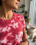 Person wearing a pink and white tie-dye shirt in a room with plants and a shelf.
