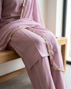 Person wearing a pink outfit with gold trim sitting on a wooden bench.