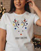 Person wearing a white t-shirt with a Christmas-themed design in front of a decorated Christmas tree.