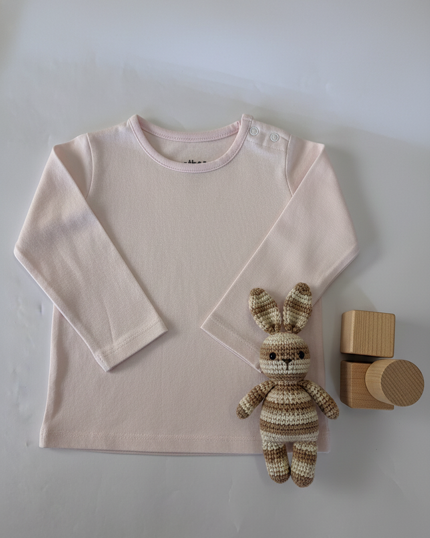 Pink long-sleeve shirt with a crocheted bunny and wooden blocks on a light gray background