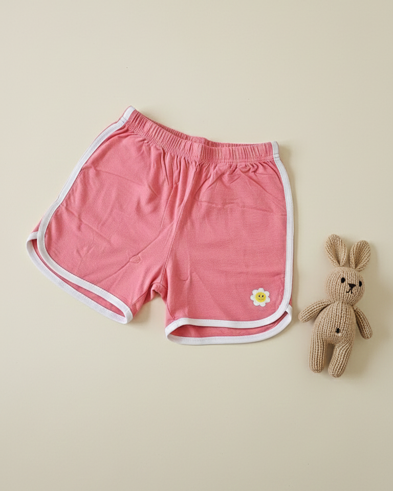 Pink shorts with a white border and a small flower design on a beige background, next to a knitted bunny toy.