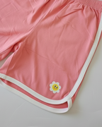 Pink shorts with a white border and a yellow flower design on a light gray background