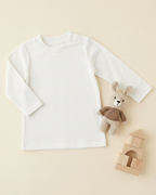 White long-sleeve shirt with a teddy bear and wooden blocks on a beige background
