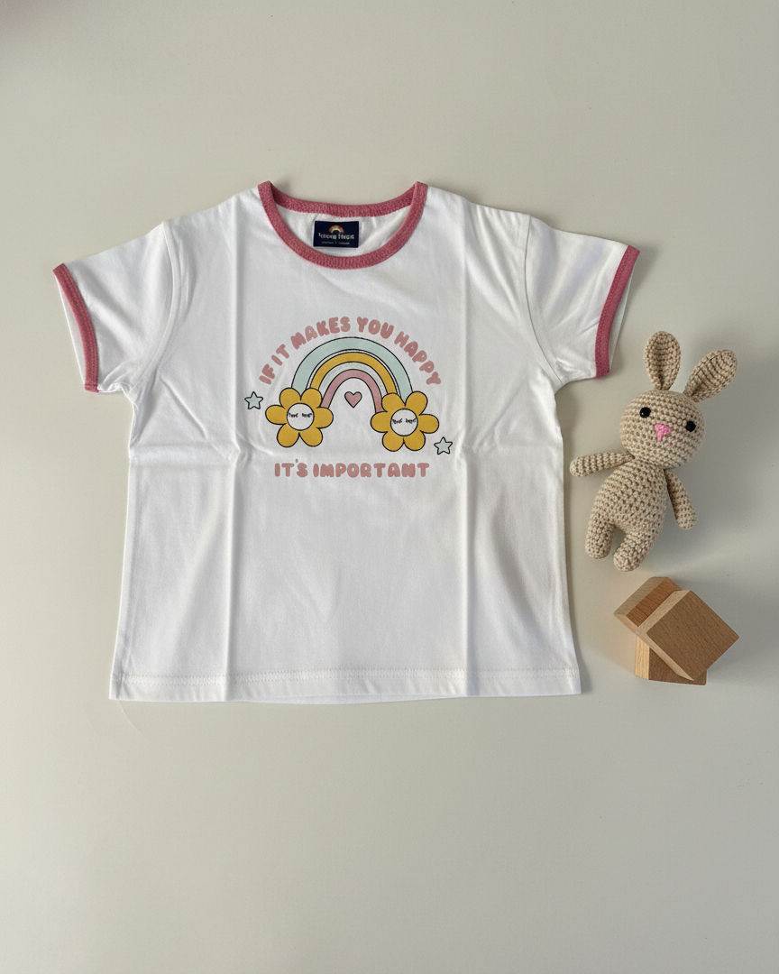 White t-shirt with colorful design and text, next to a plush toy and small box on a light gray background