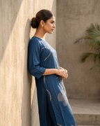 Woman in a blue outfit leaning against a textured wall.