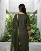 Woman in a green outfit standing in a modern indoor space with plants