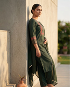 Woman in a green traditional outfit standing against a wall outdoors.