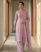 Woman in a light pink traditional outfit standing in a well-lit hallway.