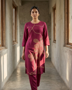 Woman in a maroon traditional outfit standing in a sunlit hallway.