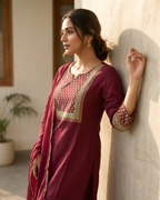 Woman in a maroon traditional outfit leaning against a wall indoors.