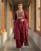 Woman in a maroon traditional outfit standing in a sunlit hallway.