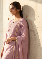 Woman in a pink traditional outfit standing against a light-colored wall.