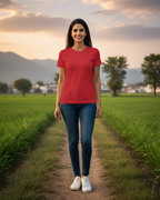 Woman in a red shirt standing on a dirt path in a green field with mountains in the background
