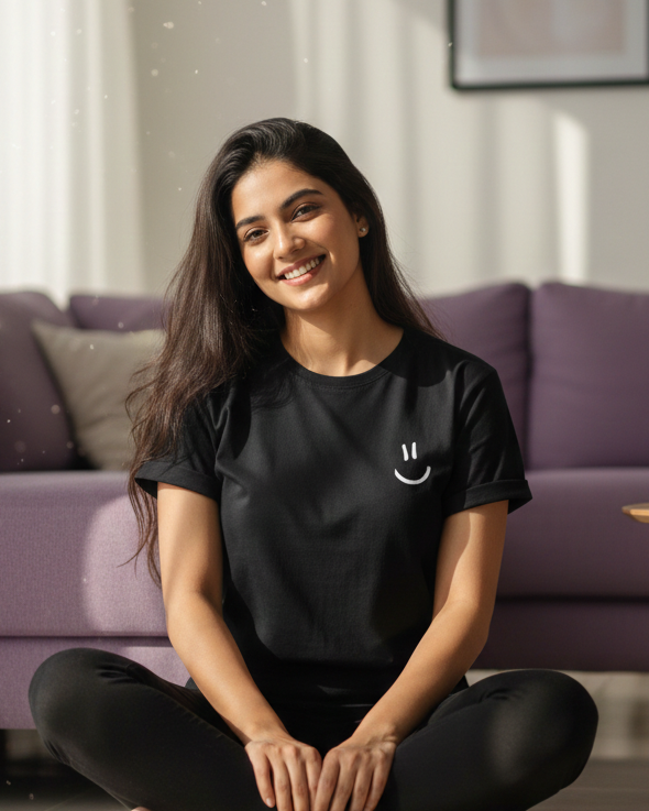 Woman sitting on the floor in a living room wearing a black outfit with a smiley face design.