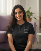 Woman sitting on the floor wearing a black t-shirt with a logo, smiling at the camera.