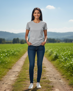 Woman standing on a dirt path in a green field with mountains in the background