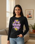 Woman wearing a black long-sleeve shirt with 'You Grow Girl' text in a living room.