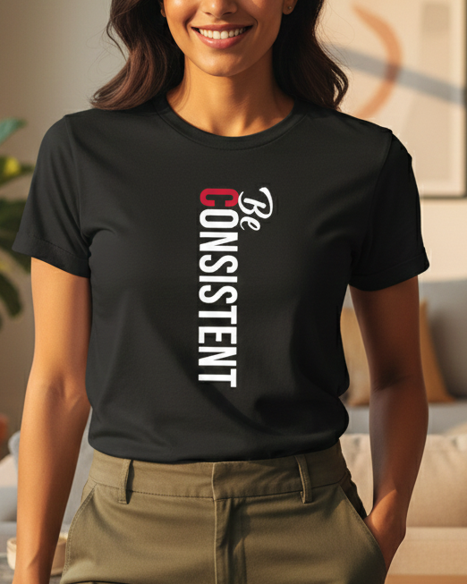 Woman wearing a black t-shirt with 'Be Consistent' text in a living room.
