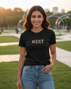 Woman wearing a black t-shirt with 'NEXT' printed on it, standing outdoors.