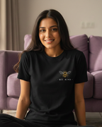 Woman wearing a black t-shirt with a bee logo sitting in a living room.