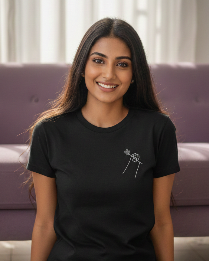 Woman wearing a black t-shirt with a small design, sitting on the floor in a room with a purple couch and white curtains.