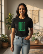 Woman wearing a black t-shirt with green text in a room with plants and a window.