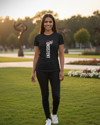 Woman wearing a black t-shirt with text standing on grass with trees in the background