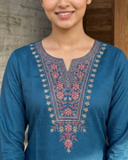 Woman wearing a blue embroidered traditional outfit standing indoors.