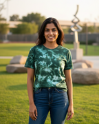 Woman wearing a green tie-dye shirt and blue jeans standing in a park.