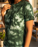 Woman wearing a green tie-dye t-shirt in a bright room with large windows.