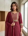 Woman wearing a maroon traditional outfit with gold embroidery in a modern indoor setting.