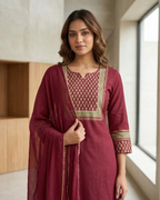 Woman wearing a maroon traditional outfit with gold embroidery in a modern indoor setting.