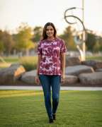 Woman wearing a tie-dye shirt and jeans standing on grass with trees in the background