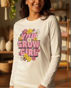 Woman wearing a white long-sleeve shirt with 'Grow Girl' text and floral designs in a home setting.