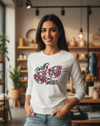 Woman wearing a white long-sleeve shirt with a colorful butterfly design and text in a store setting.